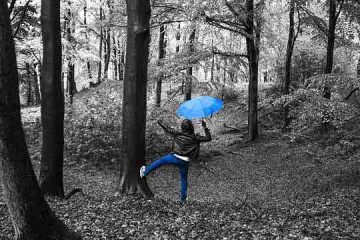 A man in the forest jumping and dancing in the rain with umbrella in hand depicting happiness, hope, and inspiration.