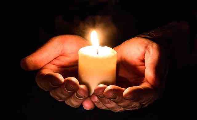 A candle in the hands and burning in the dark depicting broken heart but also hope in misery and pain.