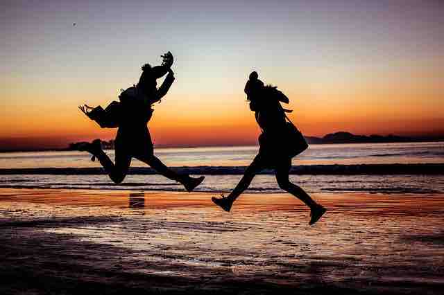 Two people jumping with joy on a beach during sunset depicting positivity, and hope for inspiring life even in dark times.