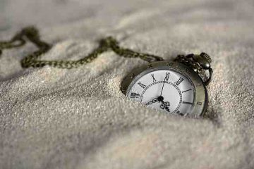 Pocket watch partially buried in the sand depicting past memories and misery.