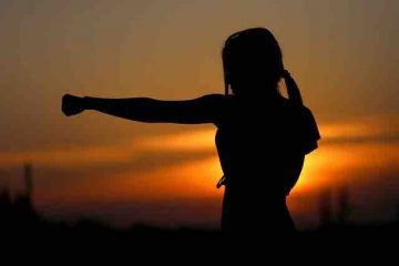 A woman boxing alone in the dawn and punching the air depicting will to overcome darkness and fighting depression.