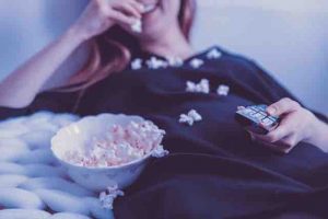 Image of a woman lying on the couch watching movie and having popcorn.