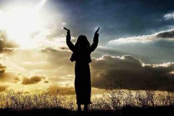 A woman looking at the sunrise and praying with hands up in the air depicting healing and hope.