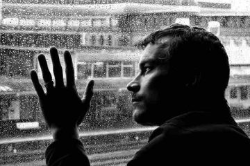 A depressed man looking at the rain out of the window showcasing thoughts about past and the pain and misery they bring.