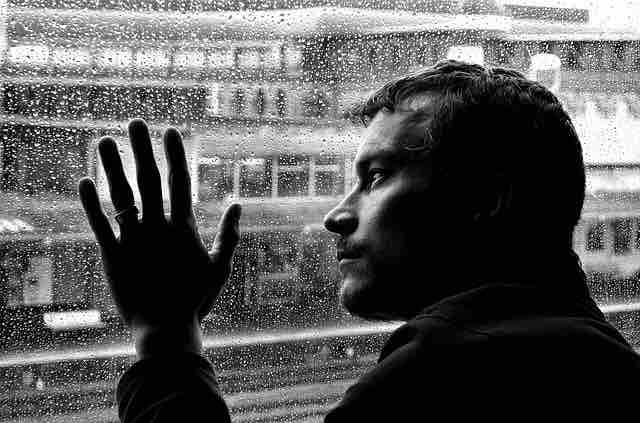 A depressed man looking at the rain out of the window showcasing thoughts about past and the pain and misery they bring.
