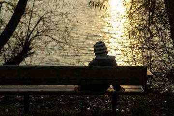 A boy sitting by the lake alone and watching the sunset depicting thoughts about past memories.