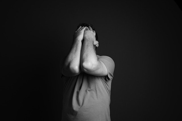 A man in the dark with hands on his face showcasing pain and misery.