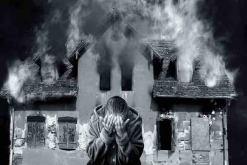 A man crying in front of a burning house depicting the scene of a song and broken memories, pain, and misery.