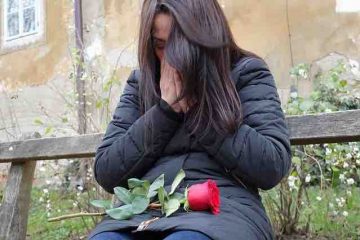 A girl crying with red rose on her lap depicting broken love, pain, and misery.