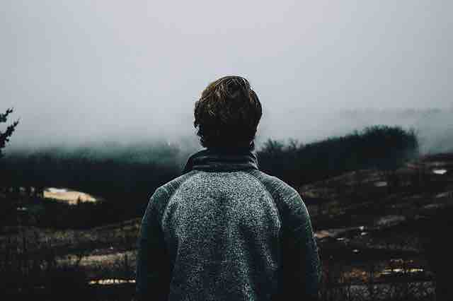 A man out in the cold under the grey skies and looking at the destruction around him depicting life and death, and misery in afterlife.