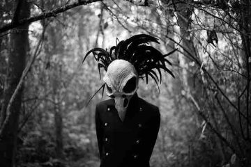 A man in a dark jungle and wearing a beak mask depicting depression, death, and darkness
