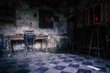 Untidy and empty dark room with only a chair and a table depicting past memories, misery and pain.