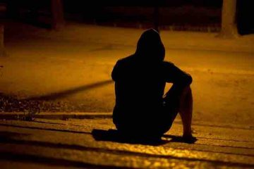 A man sitting on a footpath in the night depicting depression, misery, dark thoughts, and pain.