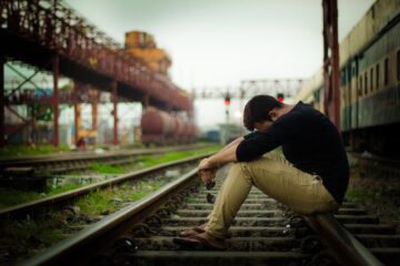 A man sitting on a railway line with head hanging depicting regrets